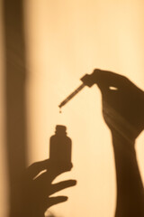 Hand holding a dropper with oil and a bottle. Shadow, silhouette. 