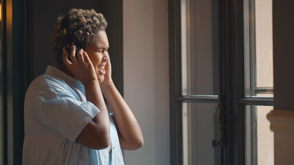 Portrait of beautiful african young woman in headphones enjoying music standing near big window