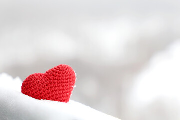 Valentine heart in the snow, background for greeting card. Red knitted symbol of romantic love in winter forest