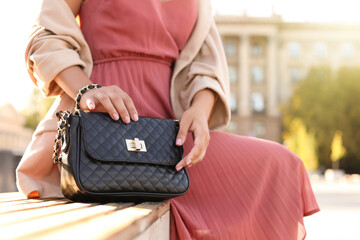 Young woman with stylish black bag on bench outdoors, closeup