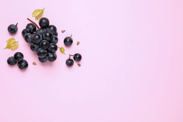Bunch of ripe dark blue grapes with leaves on pink background, flat lay. Space for text