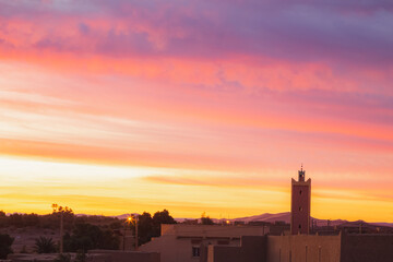 Naklejka premium A vibrant colourful sunrise or sunset over the village of Merzouga, the gateway to the Erg Chebbi desert dunes in Morocco.