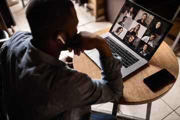 Young African American businessman looks into the laptop screen, speaks by video communication with his colleagues. Business entrepreneur, sitting in an office, pondering a business plan.
