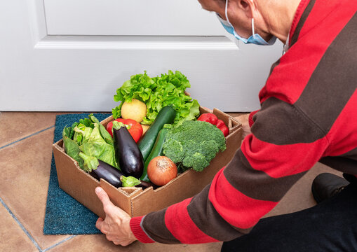 A Delivery Man Puts A Box Of Fresh Vegetables On The Floor In Front Of The Door During Quarantine And Pandemic. Food Supply Concept.