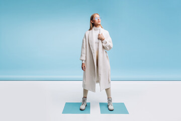 young fashionable beautiful girl in a trendy white coat and blue glasses posing on a blue background