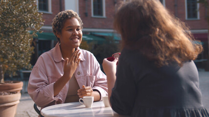 Woman holding engaged ring and making proposal to girlfriend having date in outdoors cafe