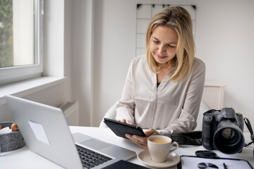 Portrait of photographer woman working home office holding camera with laptop.