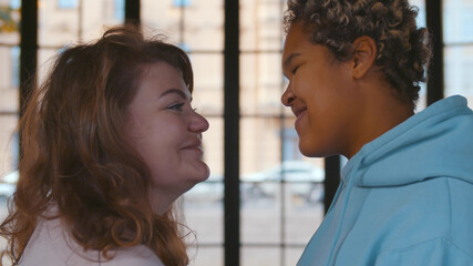 Side view of multiethnic lesbian couple indoors over panoramic window background