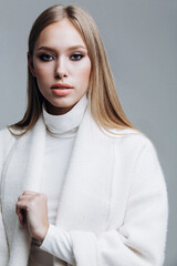 young fashionable beautiful girl in a trendy white coat posing on a gray background