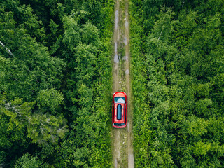 Aerial view of red car with a roof rack on a forest country road in Finland