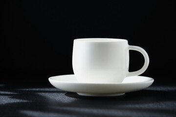 White coffee cup close-up on a black background, copy space. Coffee in the rays of the sun on a black background.