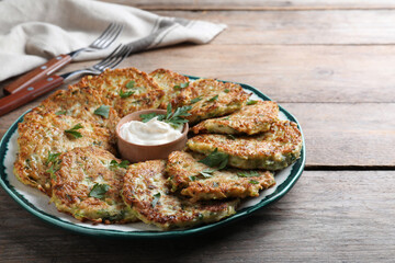 Delicious zucchini fritters with sour cream served on wooden table, closeup