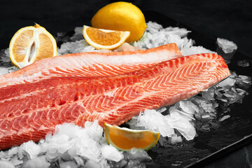 Lightly salted trout. Fresh fish fillet with culinary ingredients, herbs and lemon on a black background, side view