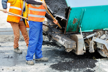 Workers use shovels to clean an asphalt paver bucket for the subsequent asphalt paving of a new section of the road.