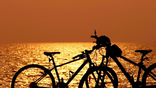 beautiful sunset view behind mtb, mountain bike, bicycle silhouette near ocean and beach with helmet for exercise outside in nature sunset time with wave and sea view