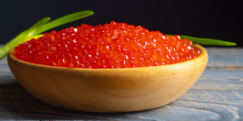 Red caviar in a wooden cup on a wooden background.