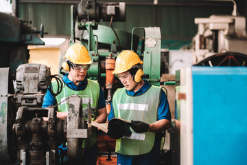 Work at factory.Two Asian workers man team working together in safety work wear with yellow helmet...