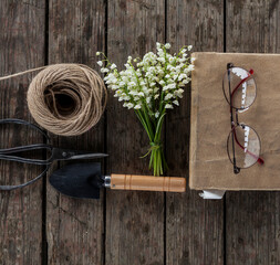 bouquet with lilies-of- the-valley,book and eye glasses on the old table in gazebo