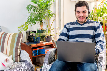 male call center agent or telemarketer in headset talking to customer working on laptop.