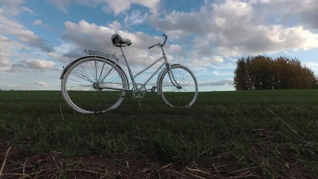 Old white bicycle on field and clouds motions, time lapse