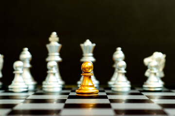 Gold pawn in chess game face with the another silver team on black background (Concept for company...