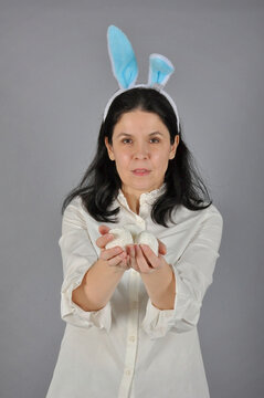 Happy smiling Easter Woman. Woman in rabbit bunny ears on head and holds an easter white eggs on grey  background
