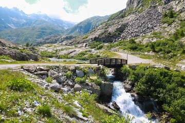 Fototapeta premium Ponte in legno che attraversa il fiume e bellissima vista sulle montagne dal sentiero che porta ai laghi Cornisello nella Val Nambrone in Trentino, viaggi e paesaggi in Italia