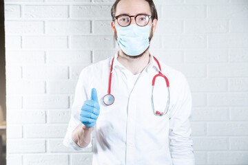 A medical worker in a protective face mask and gloves making a thumbs-up gesture.