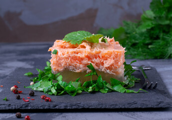 Aspic with red fish topped with herbs served in a portion piece on the gray table. Russian cuisine cold appetizer, Holodets