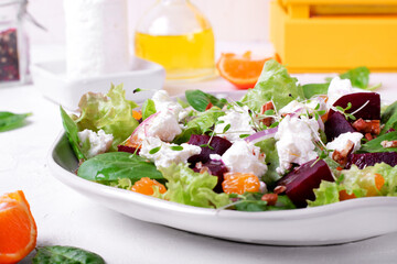 Salad with goat cheese, baked beet, tangerines, lettuce and pecan nuts served on the white plate