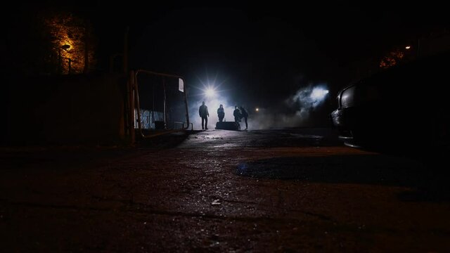 Wide shot of a group of men standing in the shadows in the night, dangerous criminals in smoke. Dangerous, urban scene.