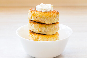Homemade cottage cheese pancakes syrniki stack on round white bowl on white rustic table background