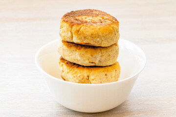 Homemade cottage cheese pancakes syrniki stack on round white bowl on white rustic table background