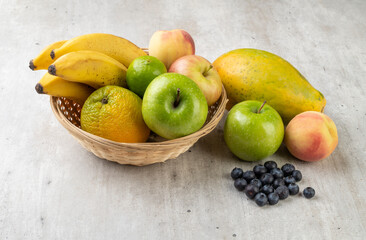 Assorted fruits in a basket over light grey table.