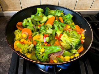 Mix of vegetables is fried in pan on stove
