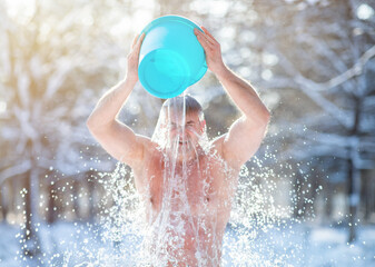 Senior man pouring water from bucket onto his head, tempering his body at snowy winter park