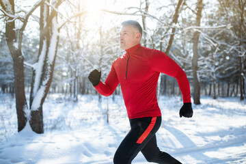 Senior athletic man in sportswear running at winter park, copy space. Seasonal outdoor sports and...