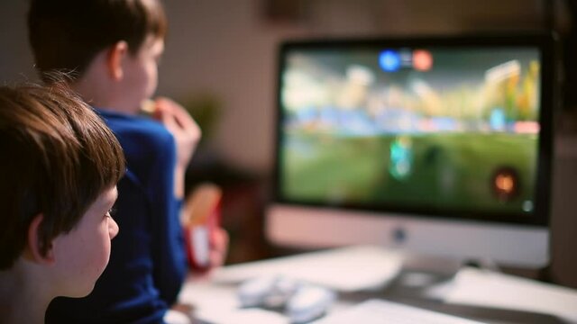 He eats snacks with his hand. The monitor shows the active picture in bokeh. Brothers Focus on the monitor. Watching a cartoon in your free time. 