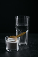 Collagen powder in bowl, glass of water and measure spoon on black background. Extra protein intake