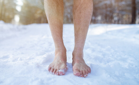 Cold training and acclimation concept. Senior guy standing barefoot on snow at winter forest, cropped view