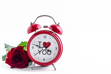 Red alarm clock with one rose on a white background. Greeting card for Valentine's Day. Copy space.