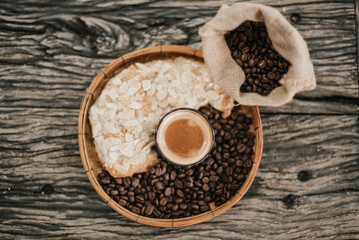 Americano coffee in a clear glass placed on a bamboo-woven tray with roasted coffee beans and croissants in the tray viewed from the top.