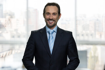 Fototapeta premium Portrait of smiling mature businessman in office. Huge blurred office windows on the background.