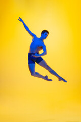 Flying, jumping. Young and graceful ballet dancer on yellow studio background in neon light. Art, motion, action, flexibility, inspiration concept. Flexible caucasian ballet dancer, moves in glow.