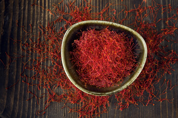 Saffron spices threads in dark bowl on dark table flat lay top view. Saffron flavor and coloring seasoning ingredient.