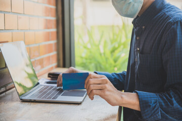 Asian man wear face mask sitting in cafe and shopping online by credit card with laptop online technology