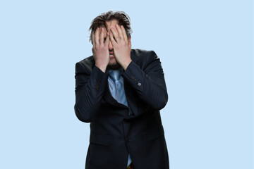 Stressed man in suit toching his face with both hands. Lose and failure concept. Isolated on blue background.