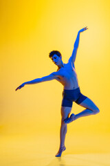 Fototapeta na wymiar Bird's freedom. Young and graceful ballet dancer on yellow studio background in neon light. Art, motion, action, flexibility, inspiration concept. Flexible caucasian ballet dancer, moves in glow.