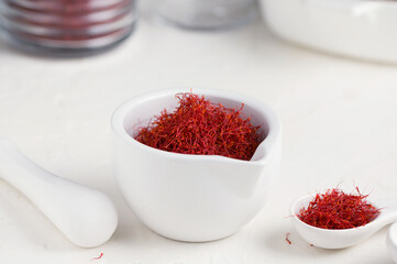 Saffron spices threads in white ceramic mortar on white table . Saffron flavor and coloring seasoning ingredient.
