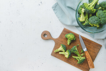 Bowl and board with fresh broccoli cabbage on light background